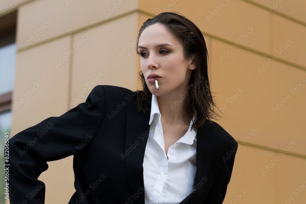 Attractive caucasian young woman in suit smoking cigarette, posing while walking outdoors on spring day. Sexy, stylish and elegant lady. Fashion, Lifestyle. Attractive caucasian young woman in suit smoking cigarette, posing while walking outdoors on spring day. Sexy, stylish and elegant lady. Fashion, Lifestyle.
