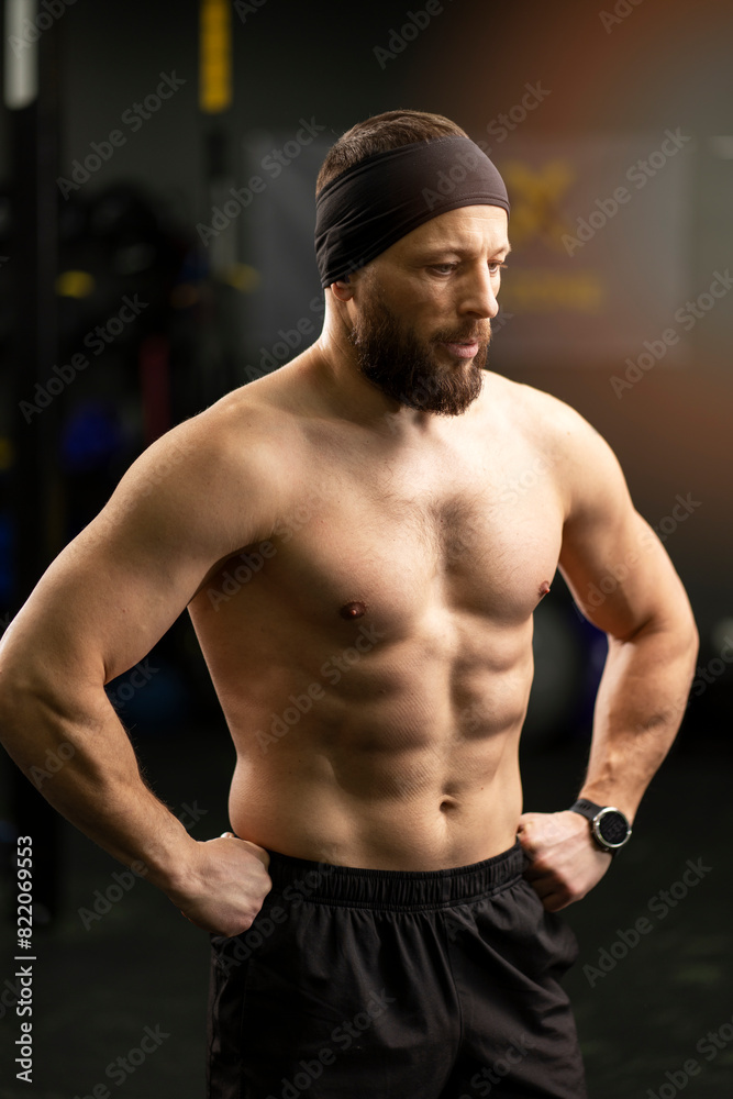 Attractive, bearded man, athlete with naked pumped up torso training in gym, standing looking away Attractive, bearded man, athlete with naked pumped up torso training in gym, standing looking away