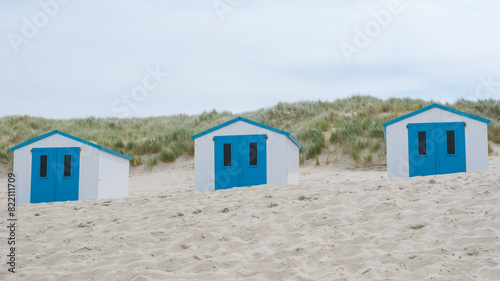 Three charming beach huts with distinctive blue doors stand out on the sandy shore of Texel, Netherlands. © Fokke Baarssen