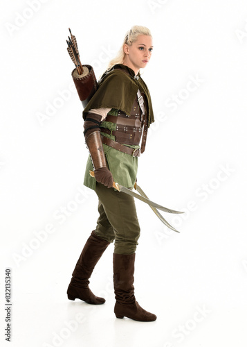 full length portrait of blonde female model wearing green fantasy elf warrior halloween costume with leather armour. standing pose, holding weapons. isolated on white studio background.