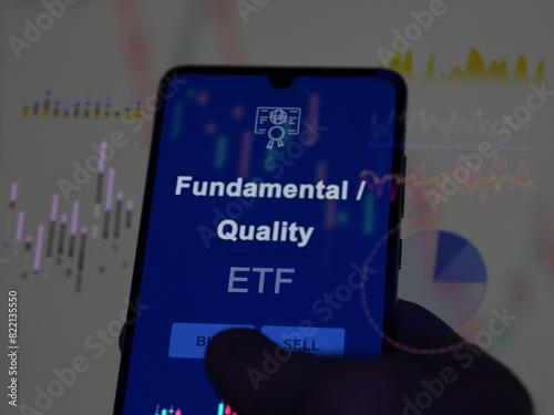 An investor analyzing the fundamental / quality etf fund on a screen. A phone shows the prices of Fundamental / Quality