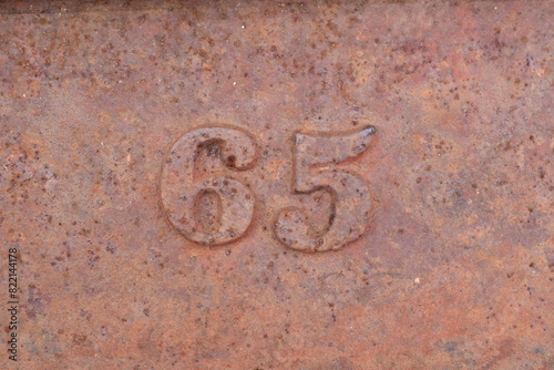 Rusty metal numbers (65) on a weathered piece of cast iron from an old sawmill