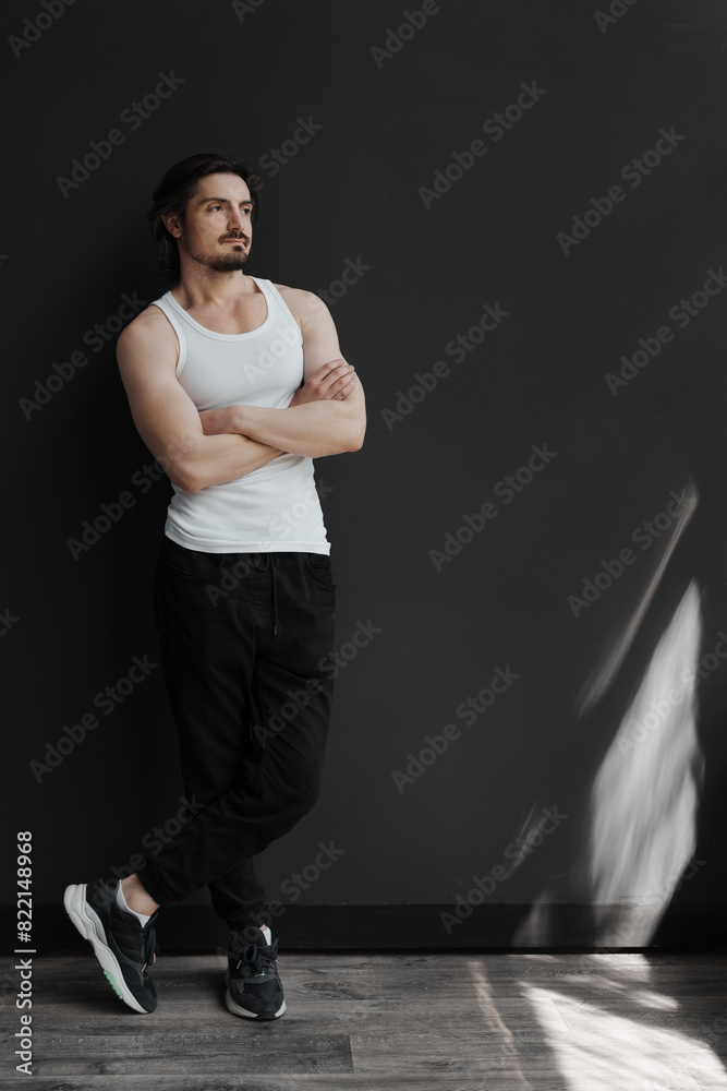 A confident man in casual clothing leans against a dark wall, exuding a relaxed and contemplative vibe.