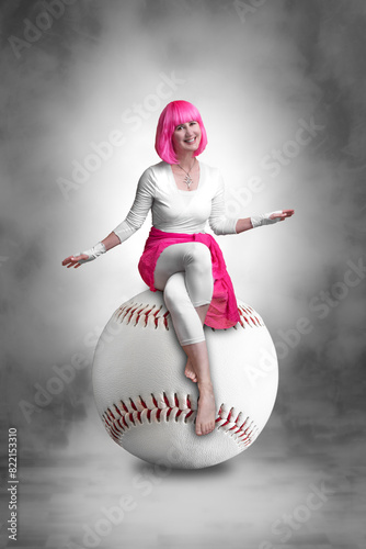 Portrait of a young woman with pink hair sitting on a giant baseball