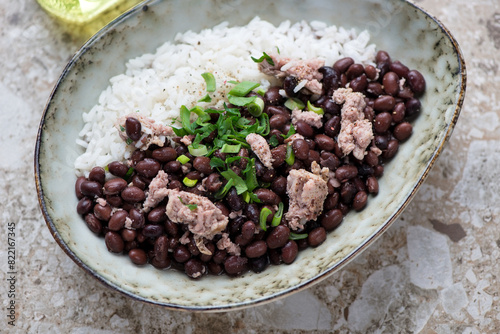 Bowl of black beans with chicken meat and white rice, horizontal shot on a light-brown granite background