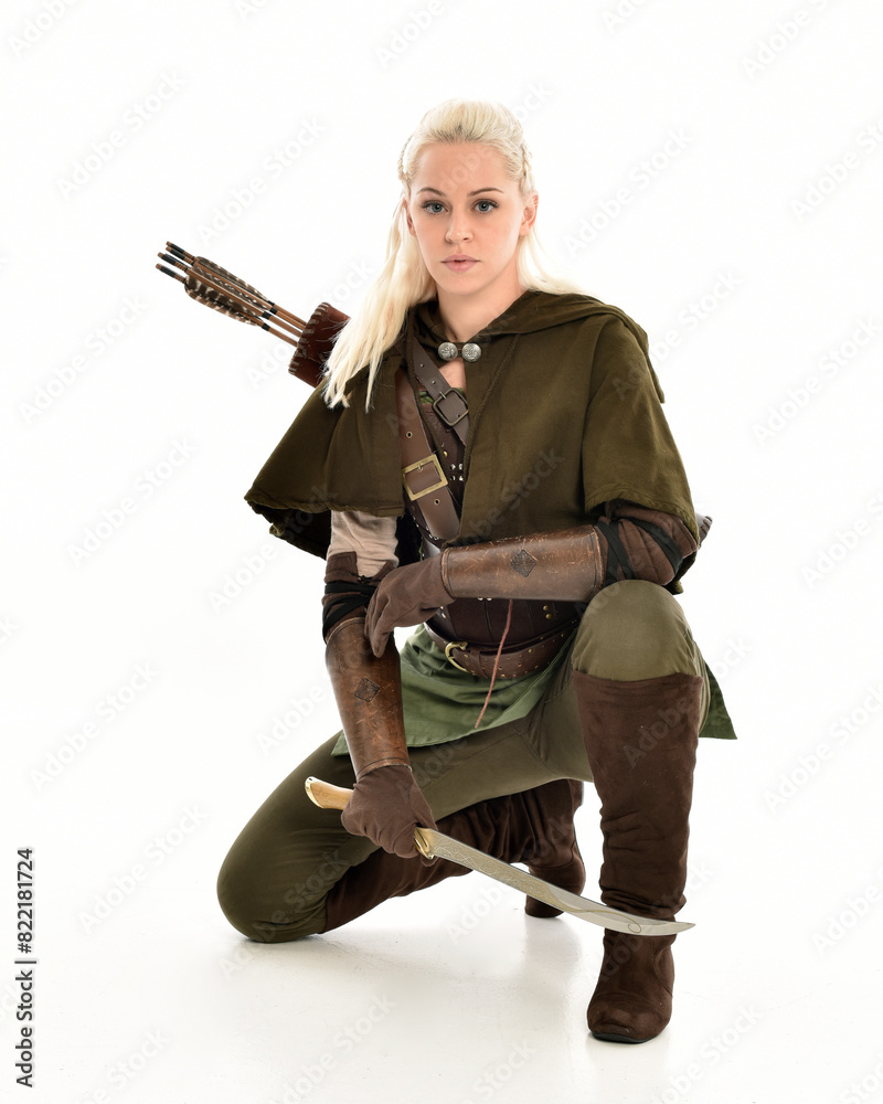 full length portrait of blonde female model wearing green fantasy elf warrior halloween costume with leather armour. sitting pose kneeling. isolated on white studio background.