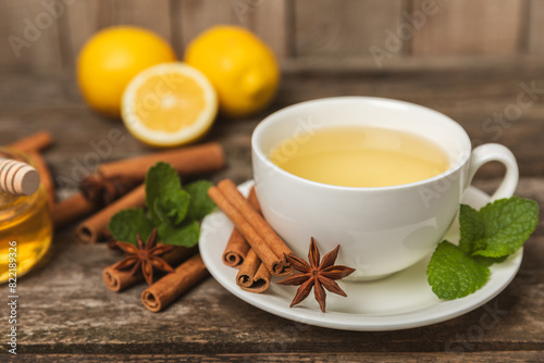 Fragrant hot tea with cinnamon stick and anise on a textured wooden background. A cup of hot tea with honey, lemon, mint and apples. Spicy tea with spices. Immunity tea. Health concept.Copy space.