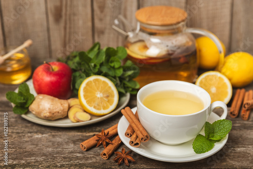 Fragrant hot tea with cinnamon stick and anise on a textured wooden background. A cup of hot tea with honey, lemon, mint and apples. Spicy tea with spices. Immunity tea. Health concept.Copy space.