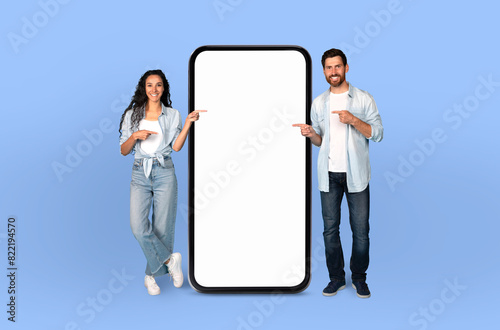 The scene features European couple, both grinning, positioned next to a life-sized smartphone mockup on a seamless blue background.