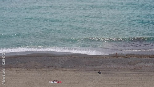 Summer aerial view of the beach with unrecognizable people sunbathing and walking carefree along the shore