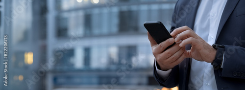 Closeup banner shot of business man hands using app holding smartphone cellphone at office building. Male entrepreneur businessman in formal suit working in trading on mobile cell phone, copy space