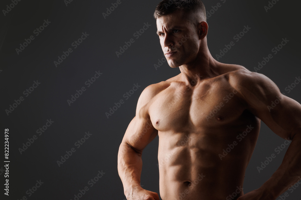 Muscular model sports young man on dark background. Fashion portrait of strong brutal guy. Male flexing his muscles.
