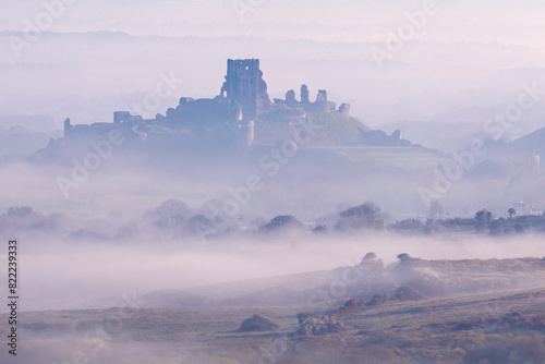 Corfe Castle, castle ruins and village, emerging from early morning mist. Photographed from Kingston, Dorset, UK. April. 
