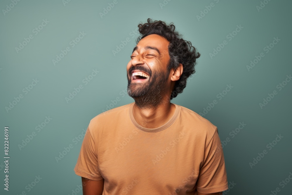 Portrait of a grinning indian man in his 30s laughing in front of blank studio backdrop Portrait of a grinning indian man in his 30s laughing in front of blank studio backdrop