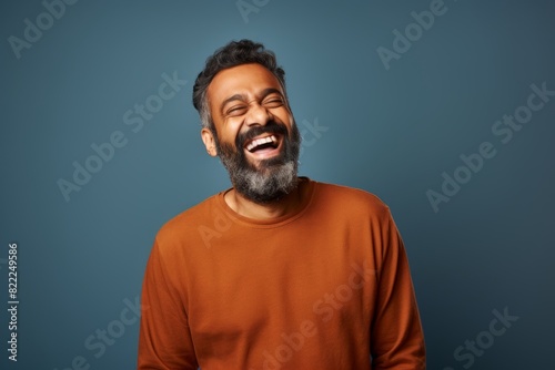 Portrait of a tender indian man in his 40s laughing in front of blank studio backdrop