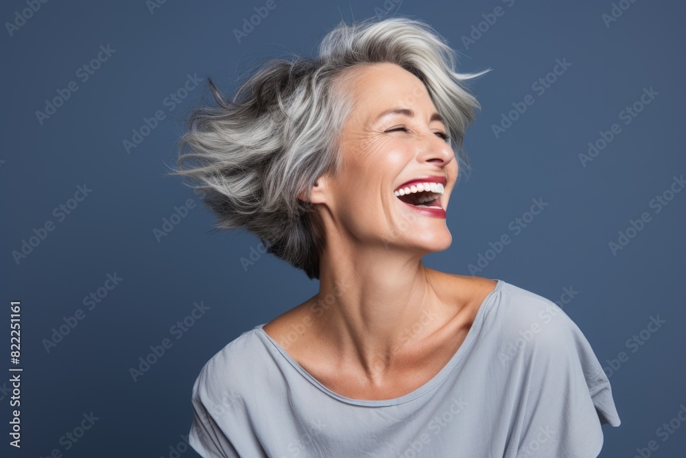 Portrait of a smiling woman in her 50s laughing while standing against blank studio backdrop