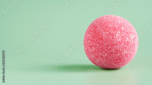 Pink sea salt bath bomb on a light green background. Porous surface of the sphere. Imitation of a mysterious ball. Copy space. Photo. Selective focus