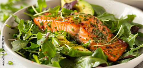 A salmon and avocado salad isolated in a white bowl  with mixed greens and a tangy vinaigrette dressing drizzled on top.