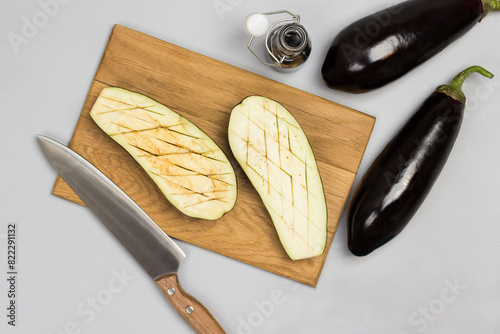 Eggplant halves on cutting board. Whole eggplants, napkin and sauce on table.