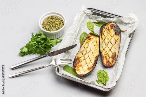 Grilled baked eggplants on pallet. Fork and knife. Mash in bowl and parsley sprigs