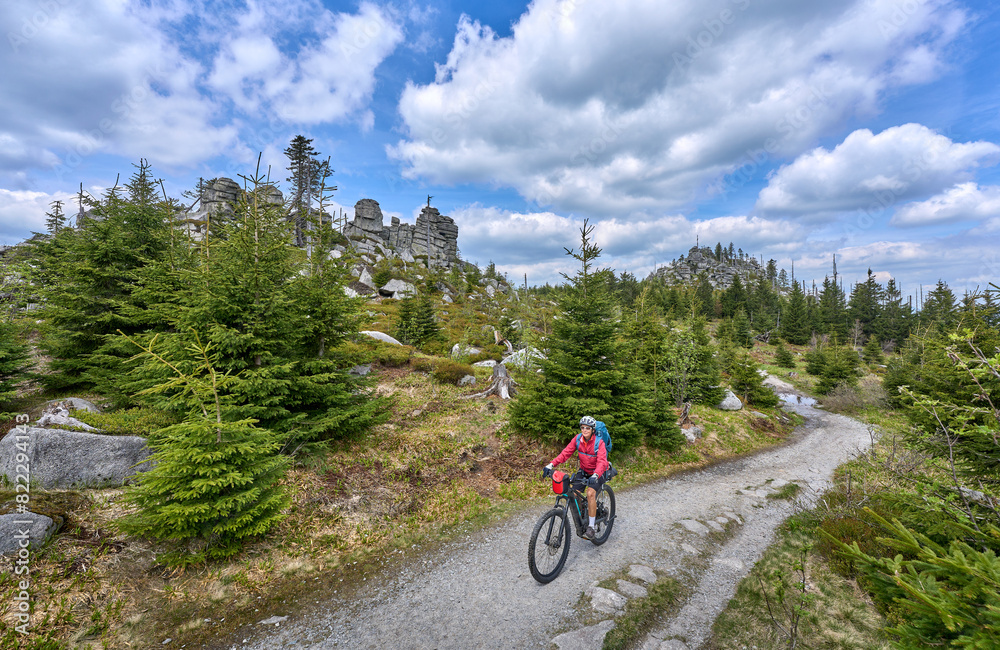 active senior woman on a bike packing tour with her electric mountain bike in the rocky the summit of Great Arber in the Bavarian Forest, Bavaria, Germany active senior woman on a bike packing tour with her electric mountain bike in the rocky the summit of Great Arber in the Bavarian Forest, Bavaria, Germany