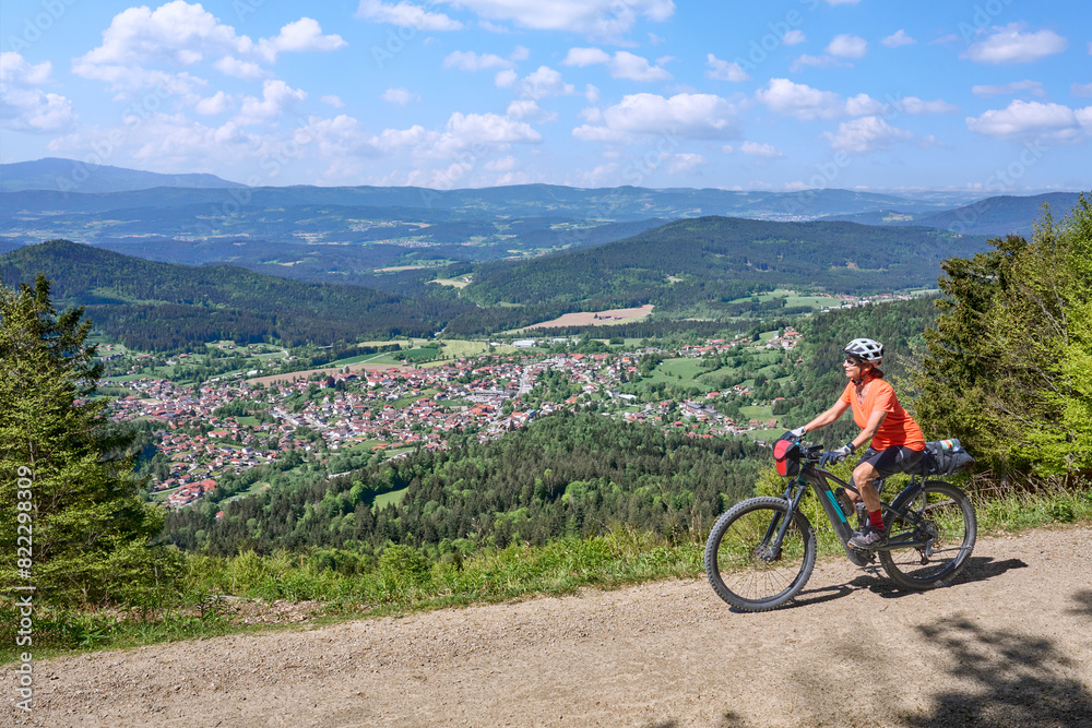 active senior woman on a bike packing tour with her electric mountain bikeup to the summit of Great Arber above village of  Bodenmais in the Bavarian Forest, Bavaria, Germany