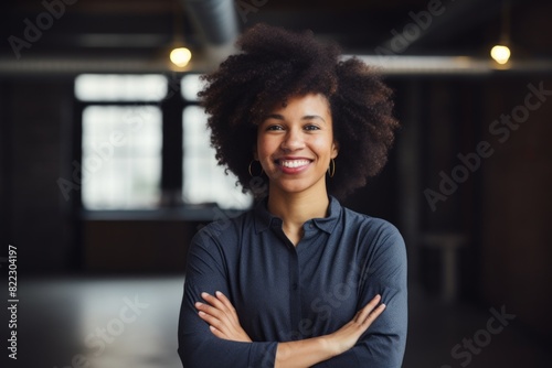 Portrait of a joyful afro-american woman in her 20s with arms crossed in front of empty modern loft background photo