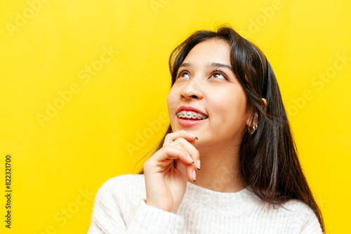 young thoughtful asian woman with braces planning and imagining on yellow isolated background, korean girl dreaming and thinking