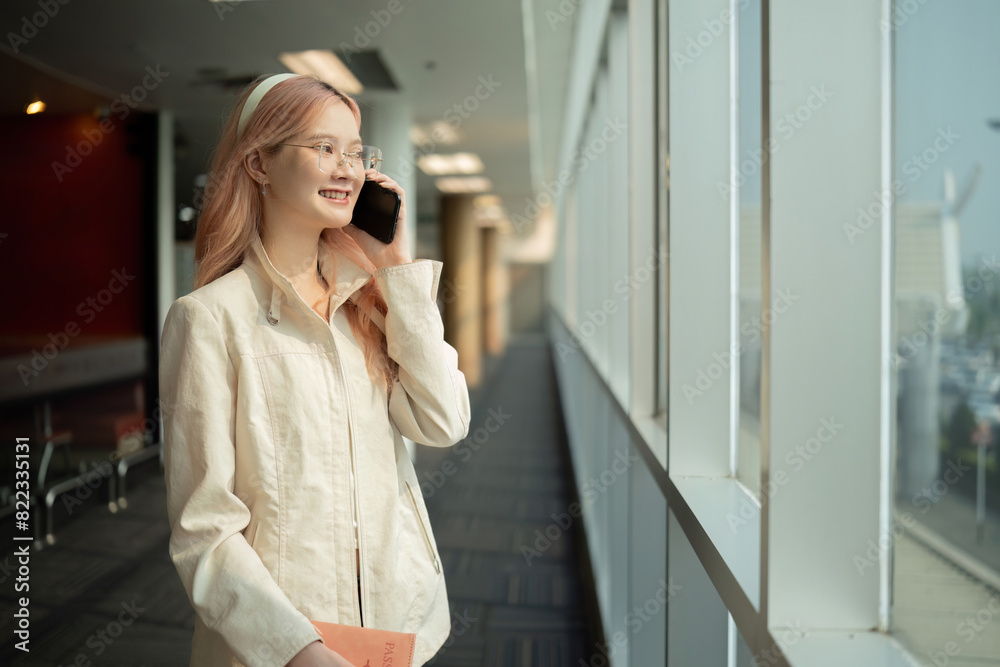 Asian woman talking on smartphone in airport terminal. Concept of travel, communication, and anticipation Asian woman talking on smartphone in airport terminal. Concept of travel, communication, and anticipation