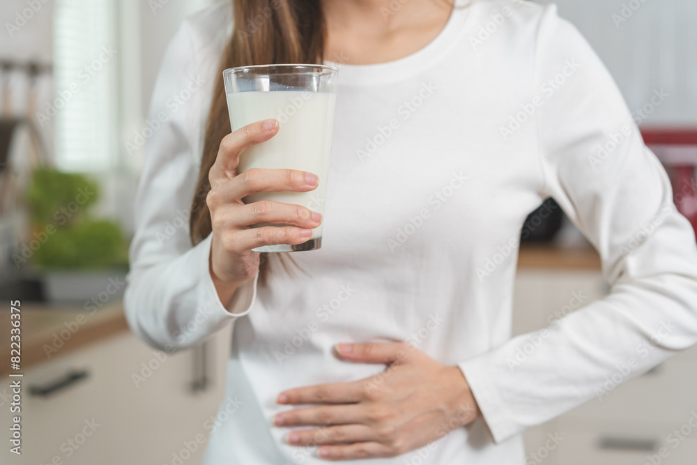 Pain, suffering asian young woman having a stomachache, abdominal pain or digestive, hand in holding belly after drink glass of milk. Lactose intolerance, allergy from dairy food, health care problem. Pain, suffering asian young woman having a stomachache, abdominal pain or digestive, hand in holding belly after drink glass of milk. Lactose intolerance, allergy from dairy food, health care problem.