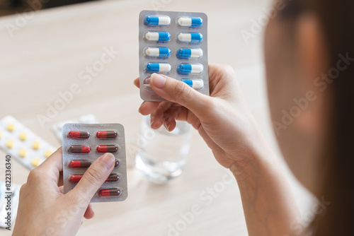 Health care treatment asian young woman holding capsules medicine pack reading label text about medical information instructions side effects at medicine on table at home, pharmacy medicament concept.