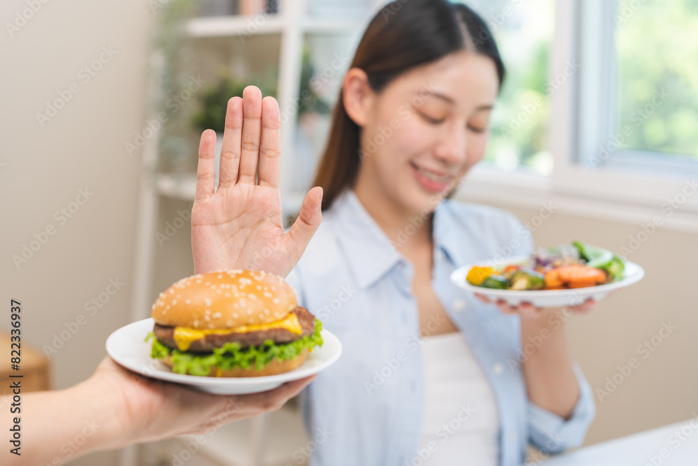 Diet concept, asian young woman hand reject eat burger, hamburger on plate, push out or deny to eat fast, junk food choose green vegetable salad, girl eat low fat for good healthy, getting weight loss Diet concept, asian young woman hand reject eat burger, hamburger on plate, push out or deny to eat fast, junk food choose green vegetable salad, girl eat low fat for good healthy, getting weight loss