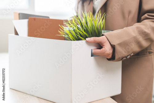 Unemployed, quite job. Desperate asian young businesswoman resigning from company, hand holding cardboard, packing belongings, stuff into box, layoff or changing work. Resignation, employment concept. photo