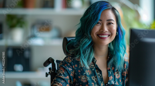 Inclusive image of female employee with blue hair sitting in a wheelchair in diverse & accessible dei workplace. Happy remote worker at computer. Pride month business marketing inclusion concept. photo
