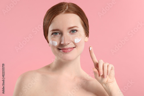 Beautiful woman with freckles and cream on her face against pink background