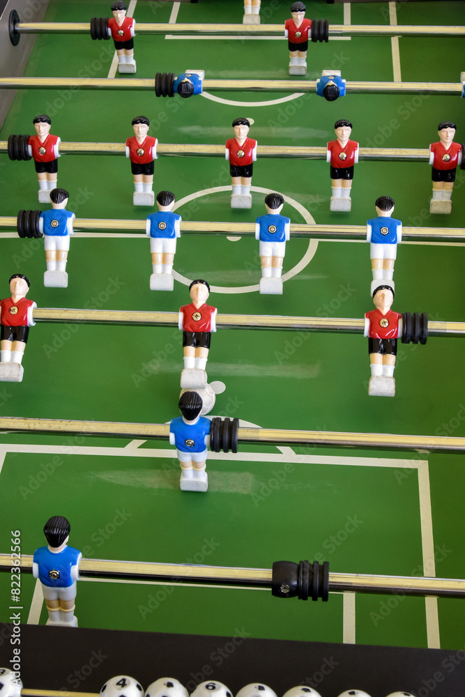 Classic Foosball Table Game With Players in Red and Blue Jerseys During Daytime Indoor Match. Close-up view of foosball table featuring red and blue jersey players positioned for daytime indoor game. Classic Foosball Table Game With Players in Red and Blue Jerseys During Daytime Indoor Match. Close-up view of foosball table featuring red and blue jersey players positioned for daytime indoor game.