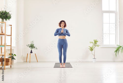 Yogi young female instructor in sportswear standing with namaste gesture  enjoying meditation practice  starting exercising for life balance  working out calm in studio  home among green houseplant