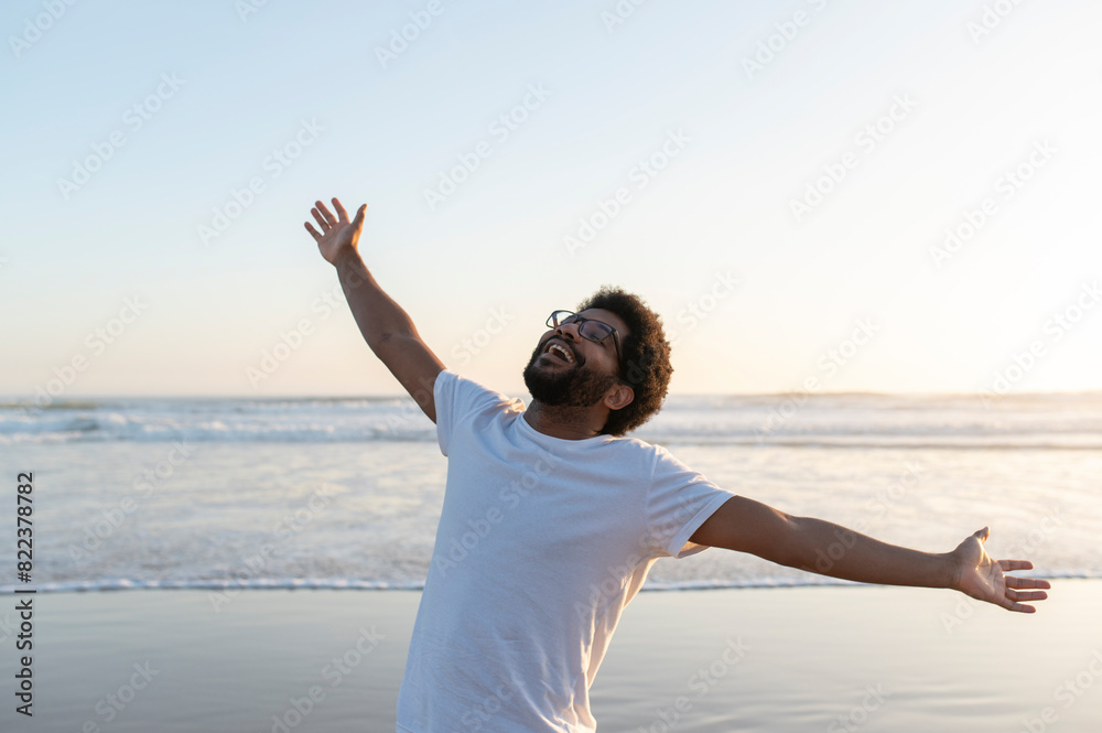 Young smiling African American man stretching his arms on the beach at the sunset, enjoying this moment Young smiling African American man stretching his arms on the beach at the sunset, enjoying this moment