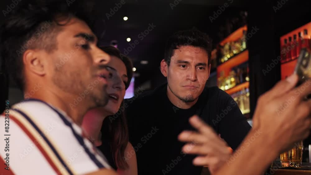 Three multiracial friends celebrating together at brewery bar. Hispanic man talks showing his phone screen. Close-up Three multiracial friends celebrating together at brewery bar. Hispanic man talks showing his phone screen. Close-up
