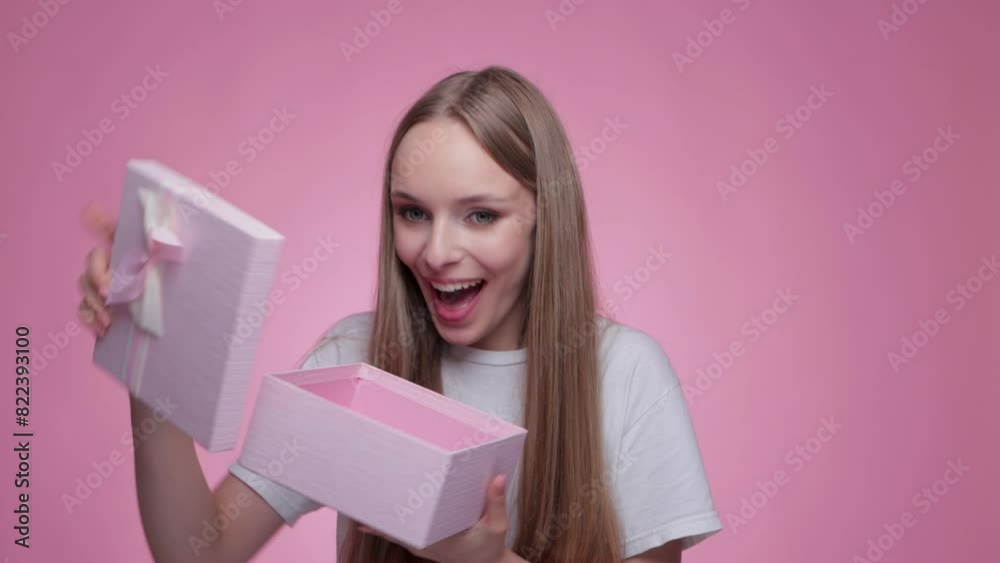 A beautiful smiling girl receives a gift in a pink box and opens it. A beautiful smiling girl receives a gift in a pink box and opens it.