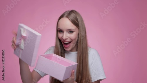 A beautiful smiling girl receives a gift in a pink box and opens it. 