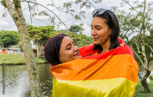 pareja lesbiana abrazadas y cubiertas por la bandera del orgullo gay  photo