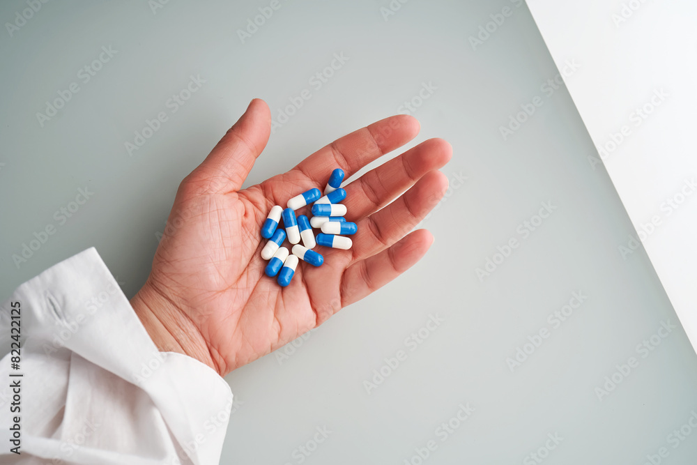 A hand holds a handful of white and blue pills on a blue background. A hand holds a handful of white and blue pills on a blue background.