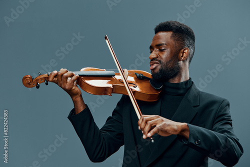 Talented African American man playing violin with passion and skill on gray background in studio setting photo