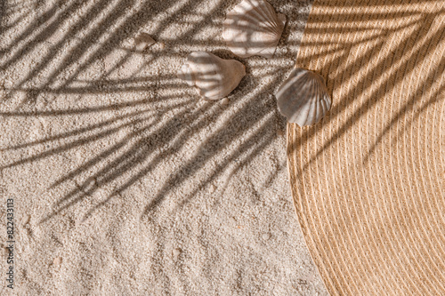 Aesthetic summer vacation and resort background, straw hat and sea shells on light beige neutral sand texture with tropical palm tree foliage sunlight shadow silhouette