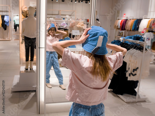 Young Woman Trying On Blue Hat in Modern Clothing Store in Afternoon