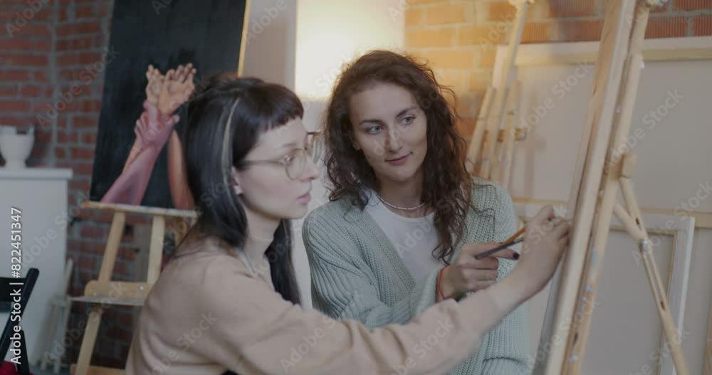 Young woman drawing and talking to art teacher enjoying individual lesson in creative studio. Visual arts and master class in workshop concept. Young woman drawing and talking to art teacher enjoying individual lesson in creative studio. Visual arts and master class in workshop concept.