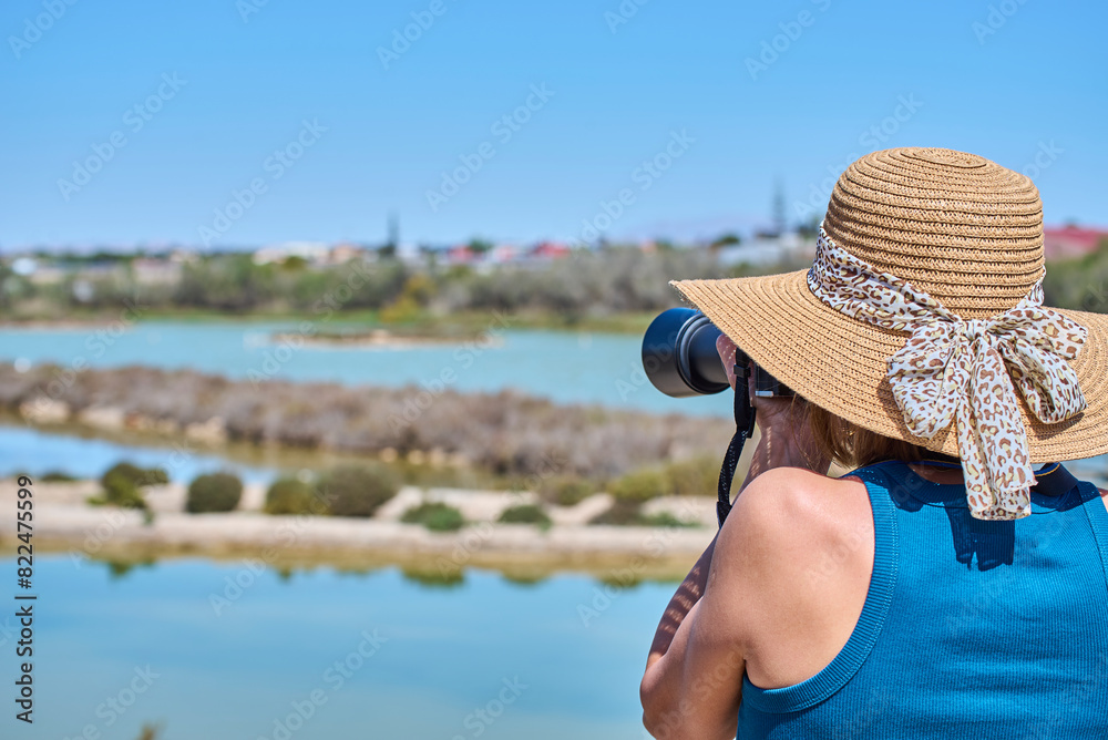 Fototapeta premium Tourist woman with summer hat taking photographs in the Santa Pola wetlands, Alicante, Valencian Community, Costa Blanca, Spain.