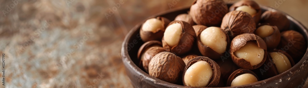 Close-up of fresh macadamia nuts in shells in a rustic bowl on a textured surface. Nutritious and healthy snack option perfect for culinary uses. Close-up of fresh macadamia nuts in shells in a rustic bowl on a textured surface. Nutritious and healthy snack option perfect for culinary uses.