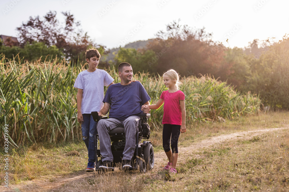 Father with disability and his children leisurely walk through natural rural surroundings and enjoy each others company. Family concept. Father with disability and his children leisurely walk through natural rural surroundings and enjoy each others company. Family concept.